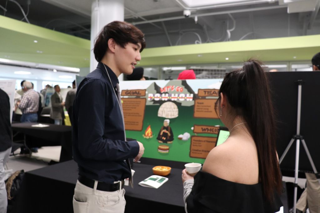 Gabriel Leung of the Let's Go Pow Wow project talks to another student Ashley Hoffman participating in the showcase about his booth in the DARE District.