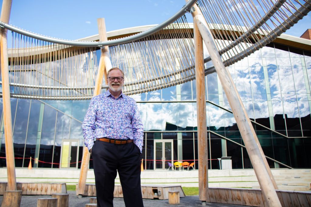 Jeff Turner, partnership development specialist with a focus on the DARE District, stands under the structure in the Ishkodewan courtyard. The structure resembles an upturned fishing weir and is one of many Indigenous aspects of the building.