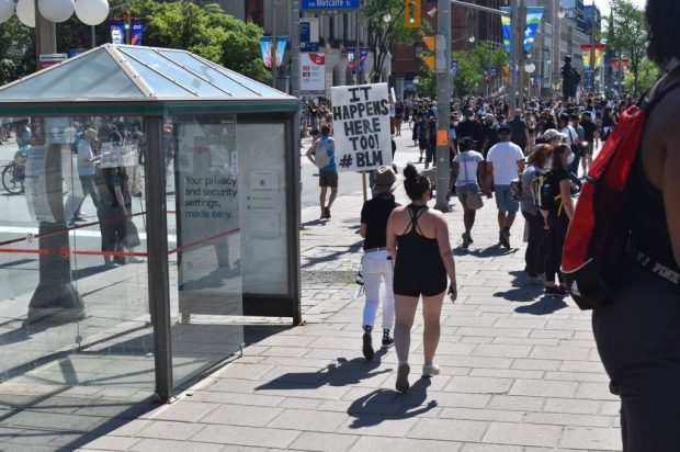 Demonstrator walks through crowd with a sign reading "It happens here too".