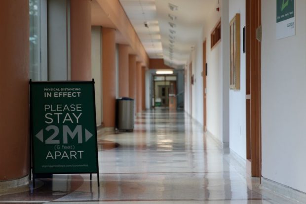 A sign asking students to stand two feet apart stands in an empty corridor