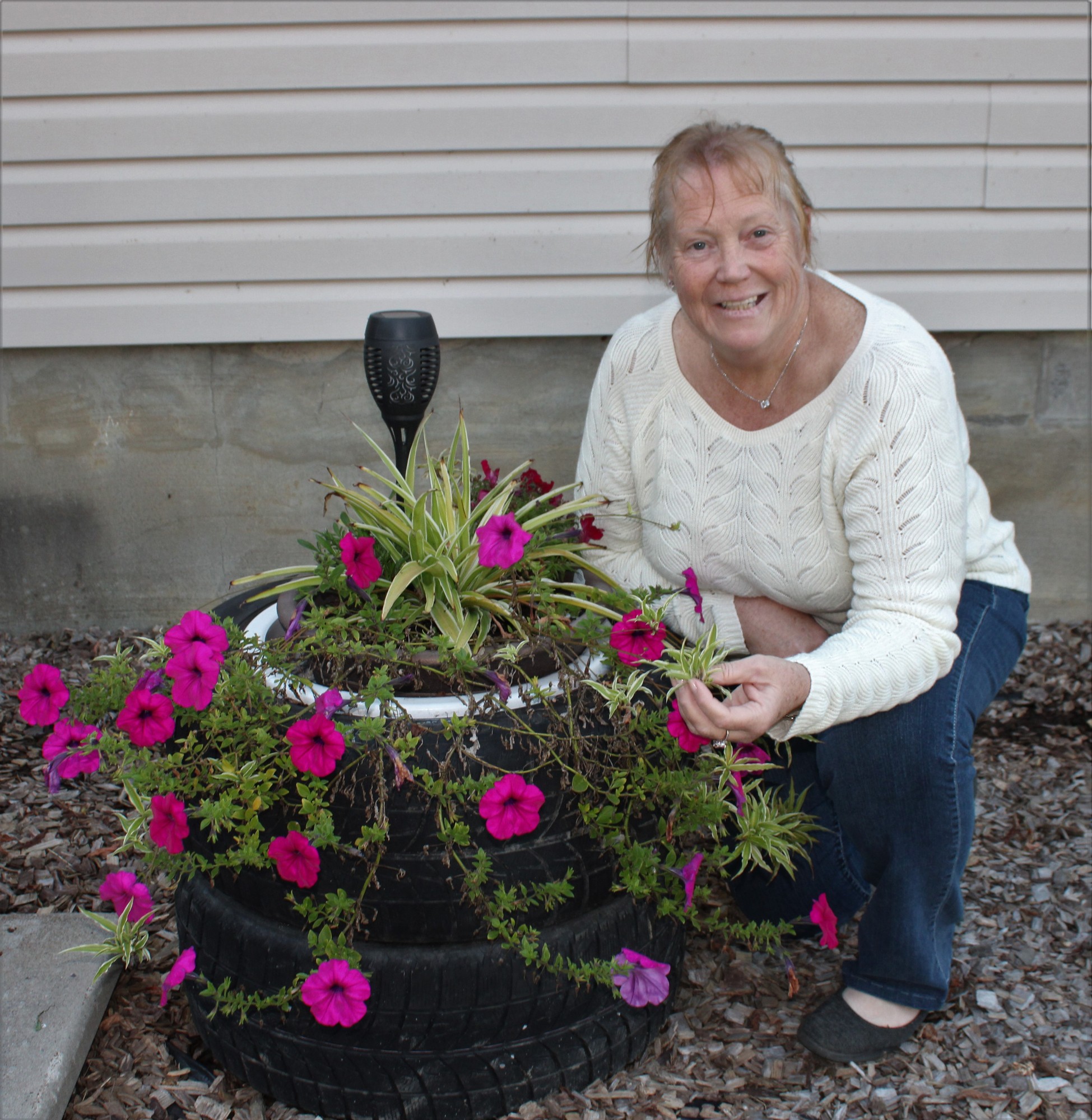 Carol Johnson, a first-semester horticulture student, enjoys spending time in her flower garden from early spring through to the last flowers of fall. She is shown with one of her recycling projects which sees a planter, made from old tires, with potted petunias and a spider plant in her front garden.