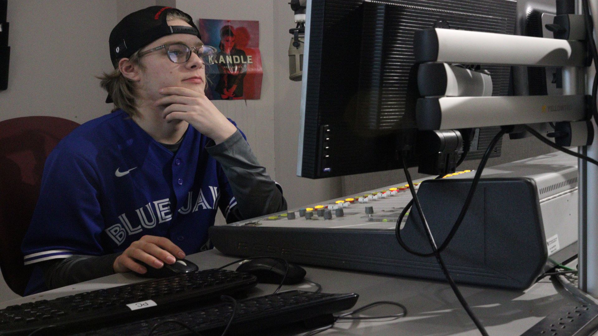 Tyler Cyr, a first-year radio broadcasting student at the college, editing audio files sporting his Blue Jays jersey with thoughts of attending baseball games this summer.