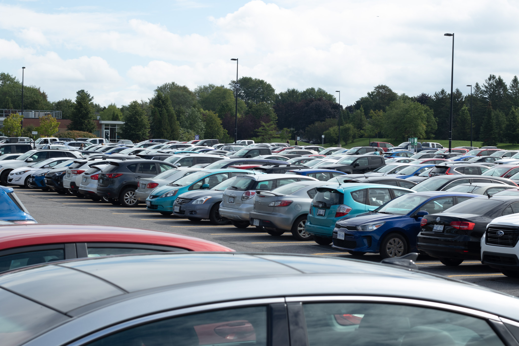 A green lot is filled with cars on a busy day.