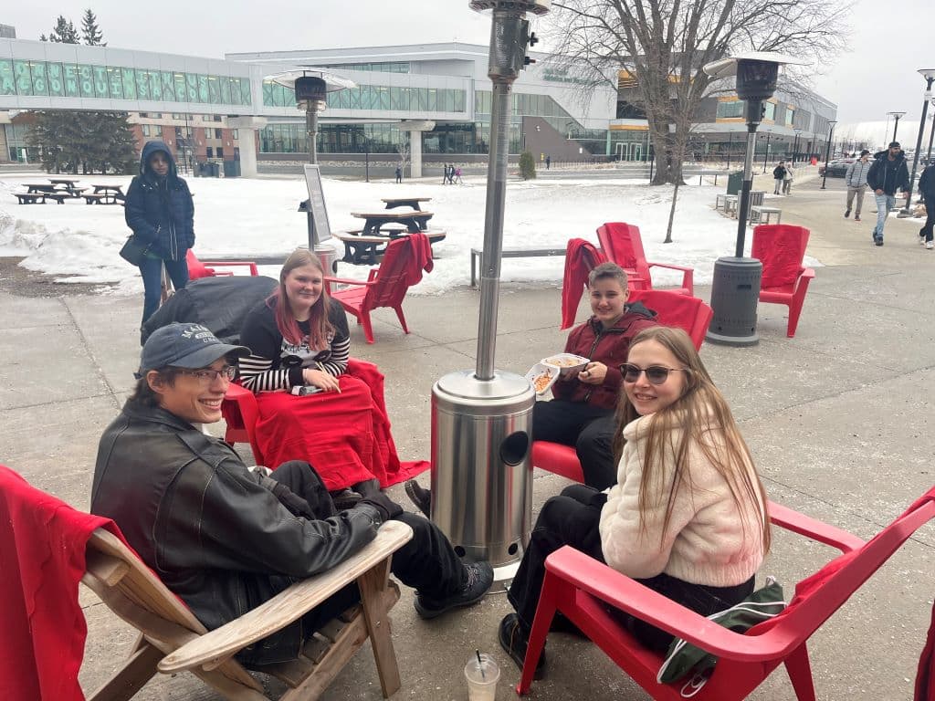 Colin Zoubak, left, Les Leeman, Logan Sudo, and Kendra Babcock, right, enjoyed the event's Muskoka chairs and keeping warm around the outdoor heater.