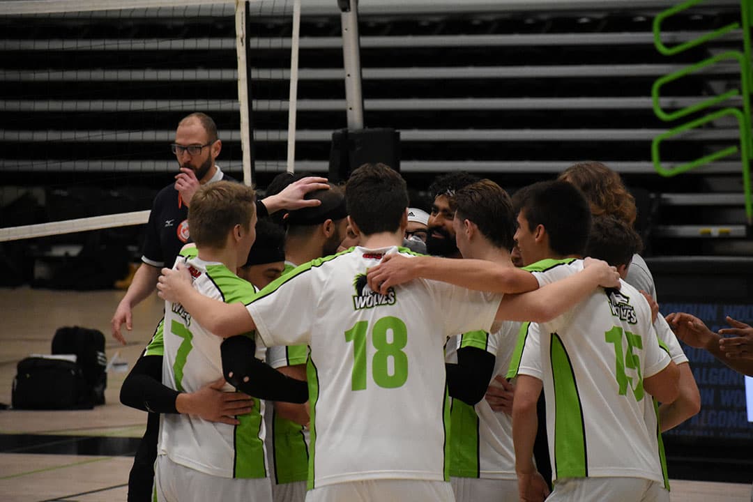 The Wolves men's team celebrates after winning its third and final set of the game against La Cité on Friday night.