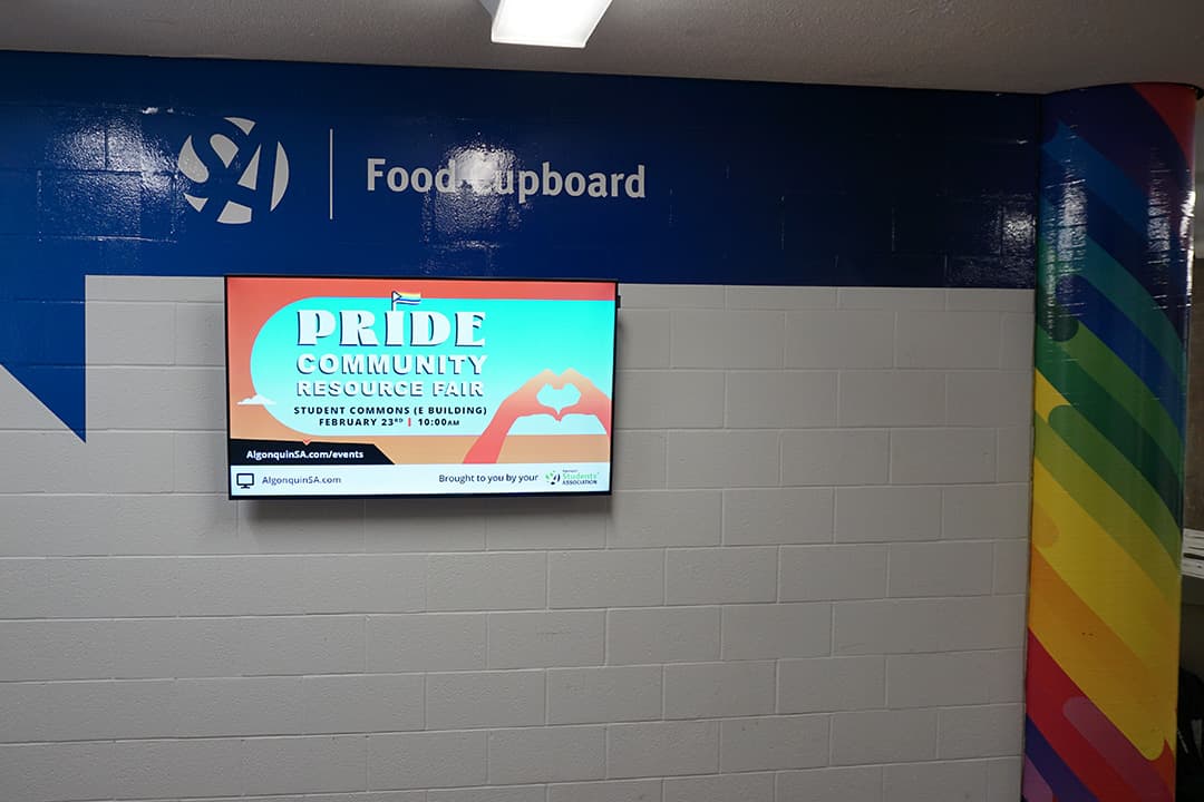 A painted sign directing people to the SA's Food Cupboard (formerly the Wellness and Equity Centre) with a pride-coloured pillar is shown on Feb. 8, 2023.