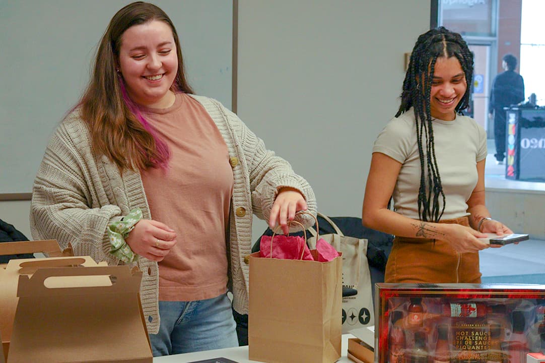 Kyla Smuck (left), and Lovishna Boodhun (right), help prepare prizes for a silent auction. Their group is organizing the great Canadian trivia night.
