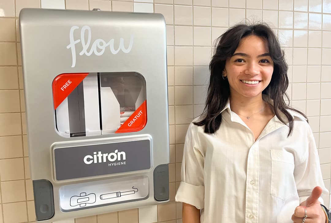 Meghan Kennedy, an advertising and marketing communications management student, stands next to a Flow menstrual product dispenser.