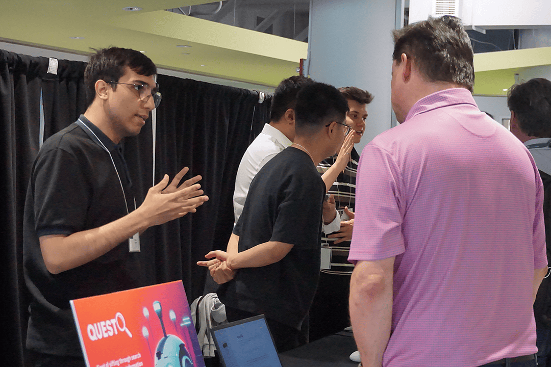 Rafael Moraes, an artificial intelligence software development student, talks with an attendee of the Re/Action Applied Research Showcase at the DARE District on April 14. His project, QuestChat, uses artificial intelligence to simplify search queries.