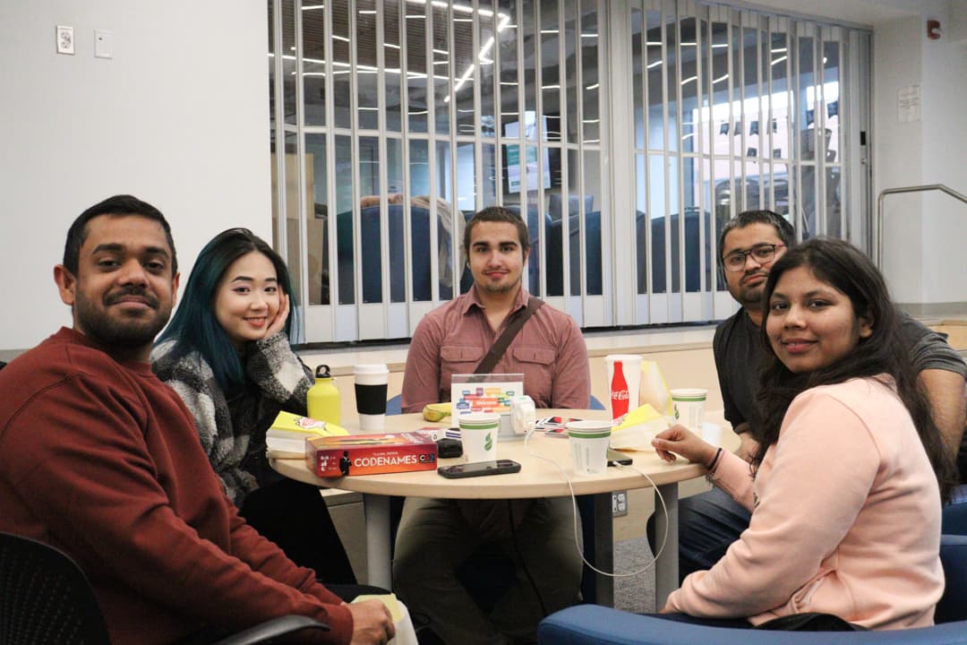 Students gather at a table during the coffee break event to play games while enjoying snacks and coffee.