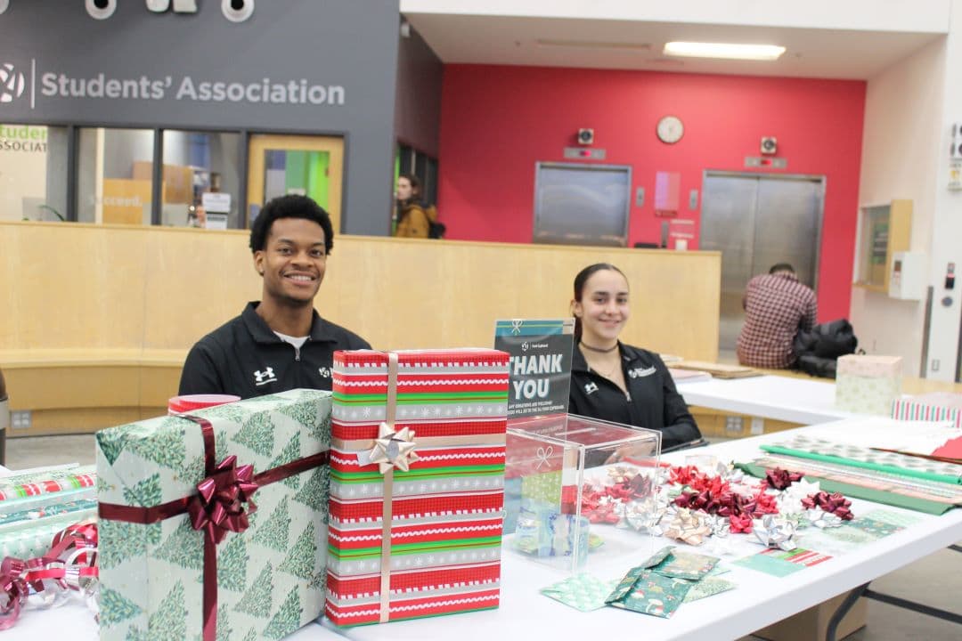 Matteo Mongroo and Veronica Sanchez offer gift wrapping services in exchange for donations to the campus Food Cupboard during the Holiday Market.