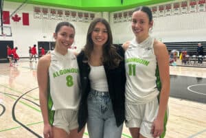 Leah, Anna and Libby Hirst, three white women with dark hair, pose after a game. Leah and Libby are in uniform, while Anna is in jeans, a white shirt and a black jacket. They are smiling at the camera.