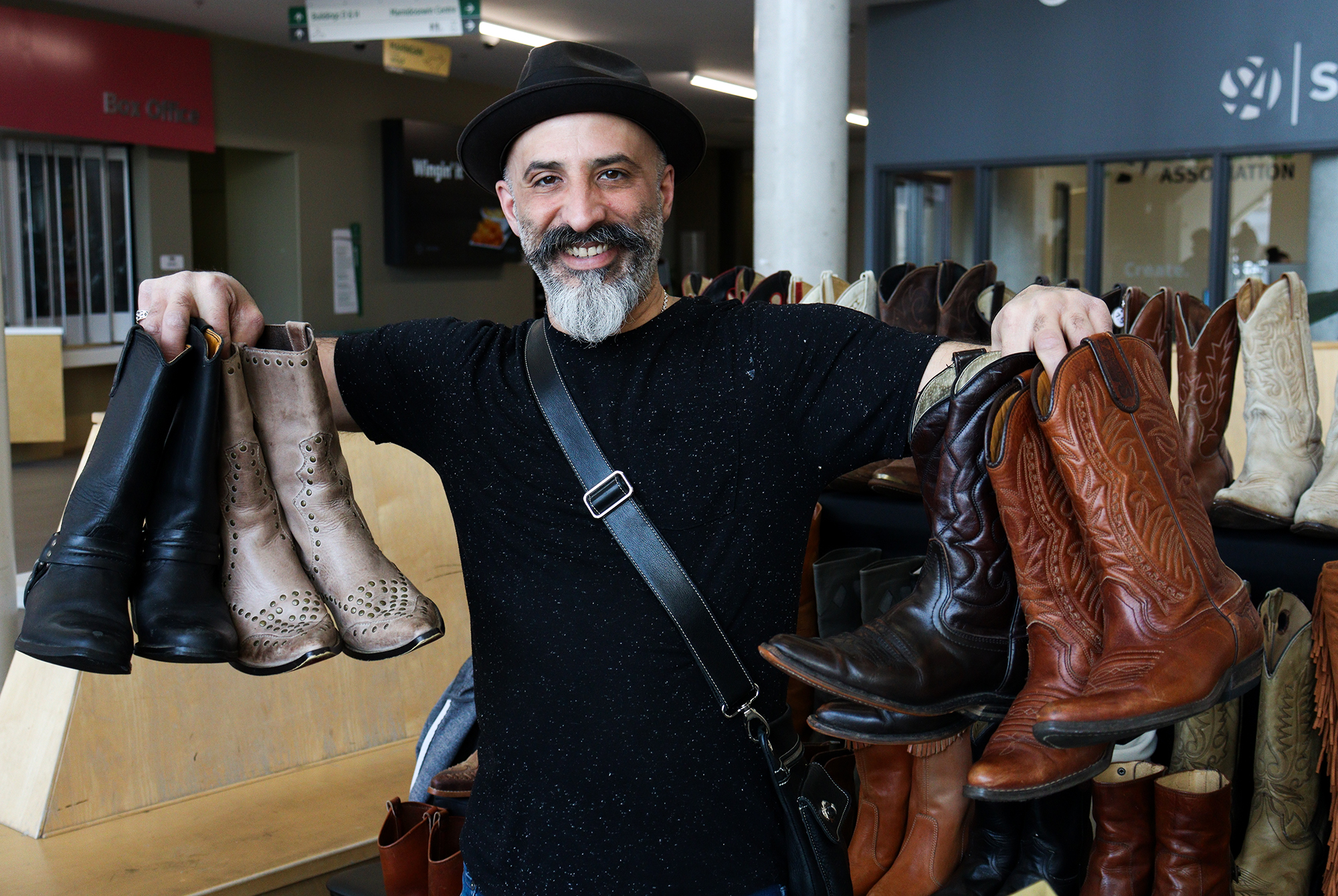 Albert Cadi, the owner of Adonis Jewellery, holds several second-hand leather cowboy boots in brown, black, and khaki at the market.
