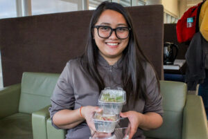 Katrina Bernasor holds up her creations from the workshop: Overnight Oats, Greek Salad with Homemade Dressing, and Guacamole, showcasing her newfound cooking skills.