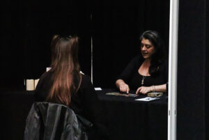 A person in a black shirt and long necklace is explaining to a student what they are curious about.