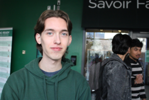 Nicolas Viau, a white man in a green sweater, looks at the camera in front of Savoir Fare