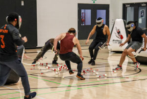 The players rush over to snatch a scattered pile of arrows on the gym floor, quickly reloading before re-engaging with the opposing team.