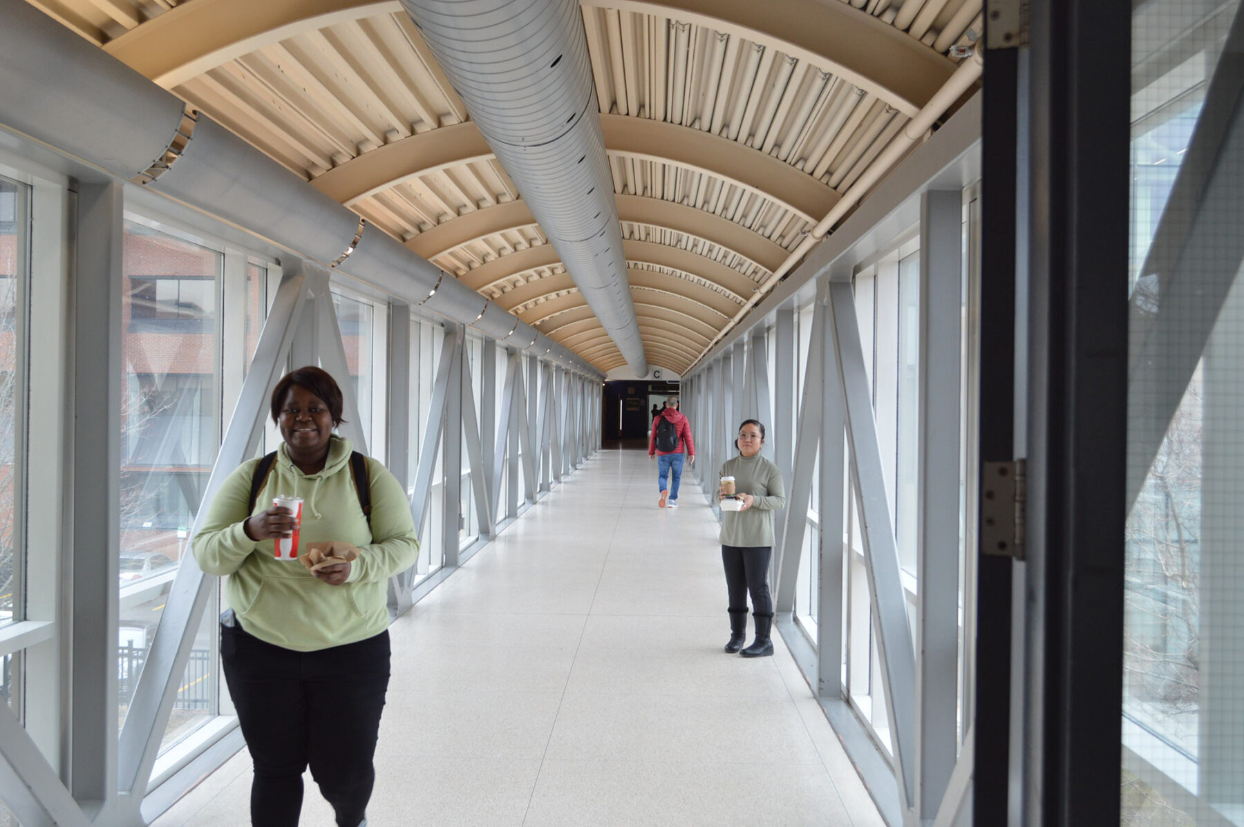 A student smiling while walking past with a drink in her hand, a student walking away and a faculty member smiling with food and drink in hand.