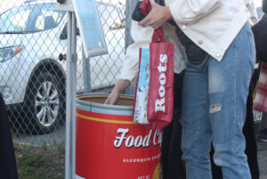 A spectator leaves a food donation in the Food Cupboard donation bin.