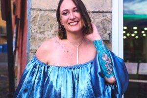 Charae Degrow poses in front of a building, smiling and enjoying herself.