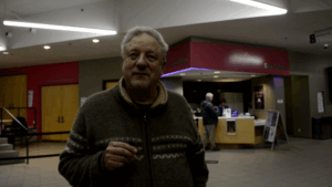 A man with short hair stands outside the Algonquin Commons Theatre, looking relaxed after answering questions.