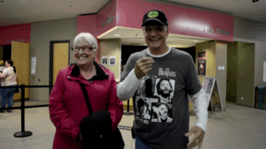 A woman and a man stand side by side outside the Algonquin Commons Theatre, smiling after completing an interview.