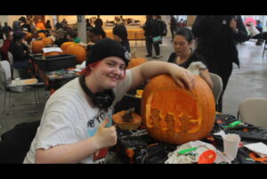 Luca Arnold poses for a photo after adding some finishing details to their Deltarune pumpkin carving in the Student Commons on Oct. 30.