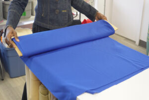 Adu shows the process of fabric donation, rolling the fabric onto a bolt.