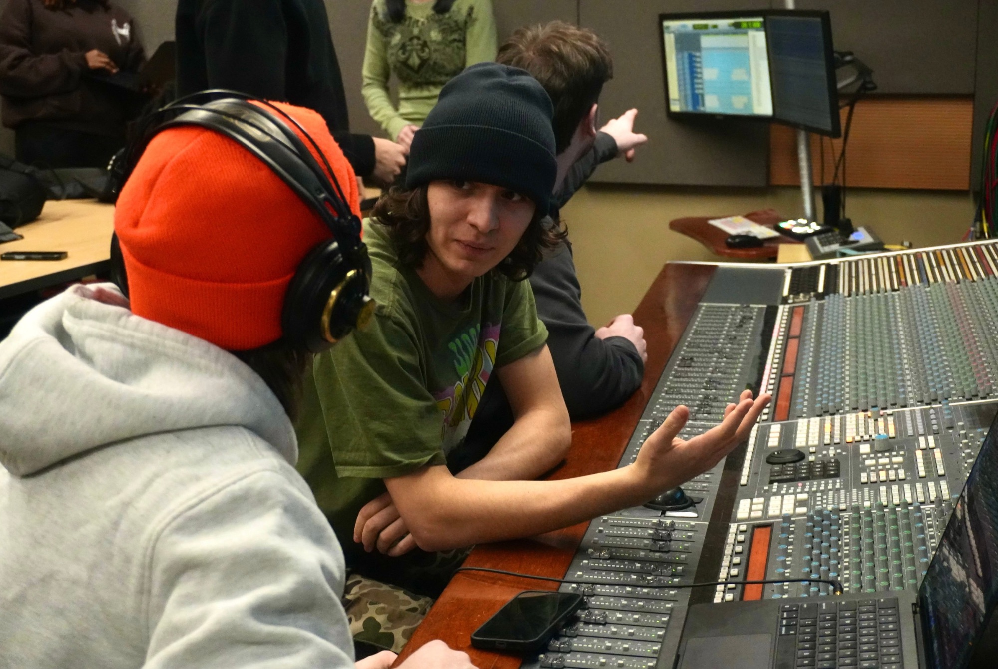 A student gestures while classmates discuss audio mixing at Algonquin College’s Music Industry Arts program, which faces possible suspension despite high graduate success.