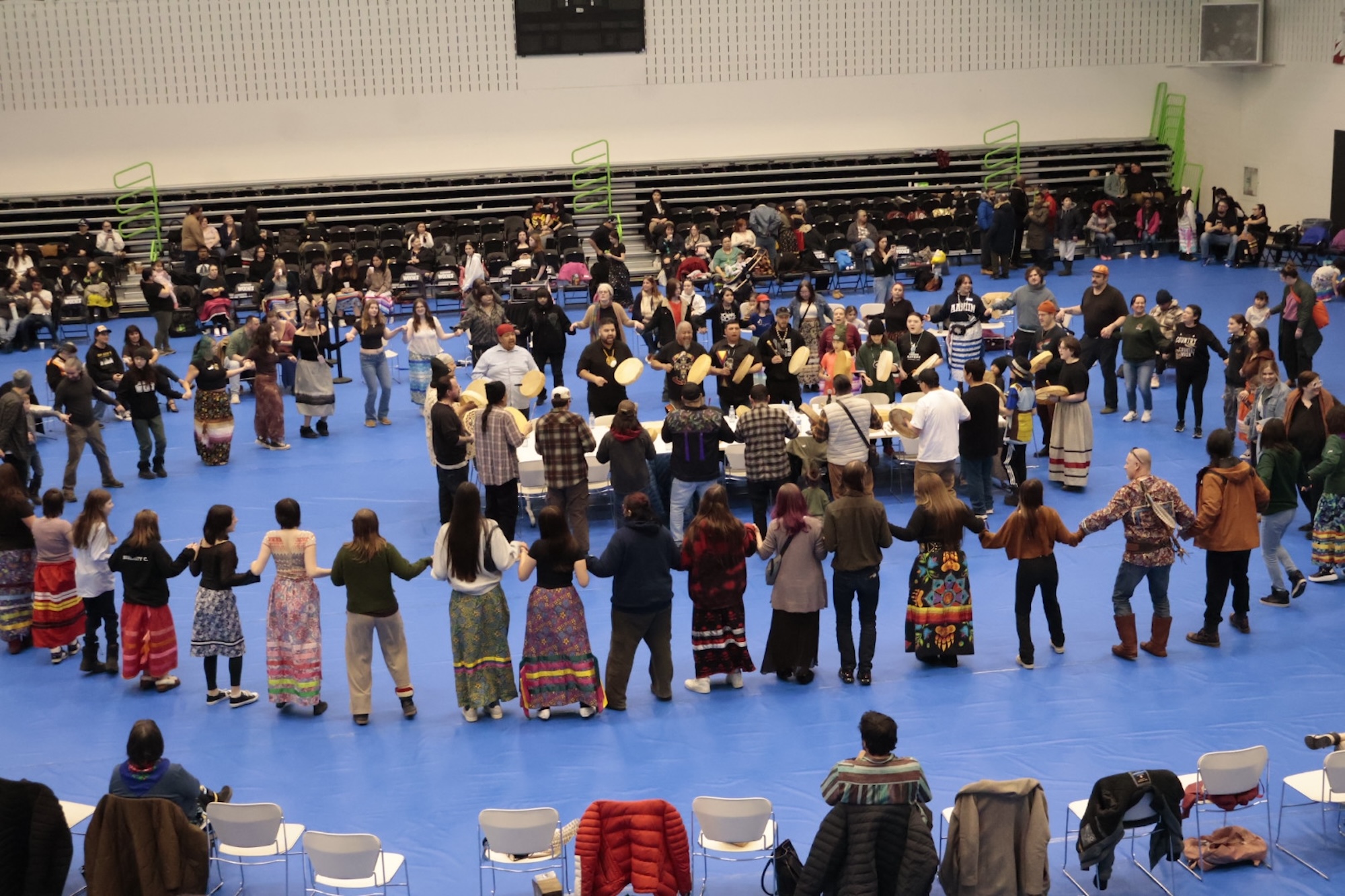 People dancing hand in hand in a circle as drummers sing.