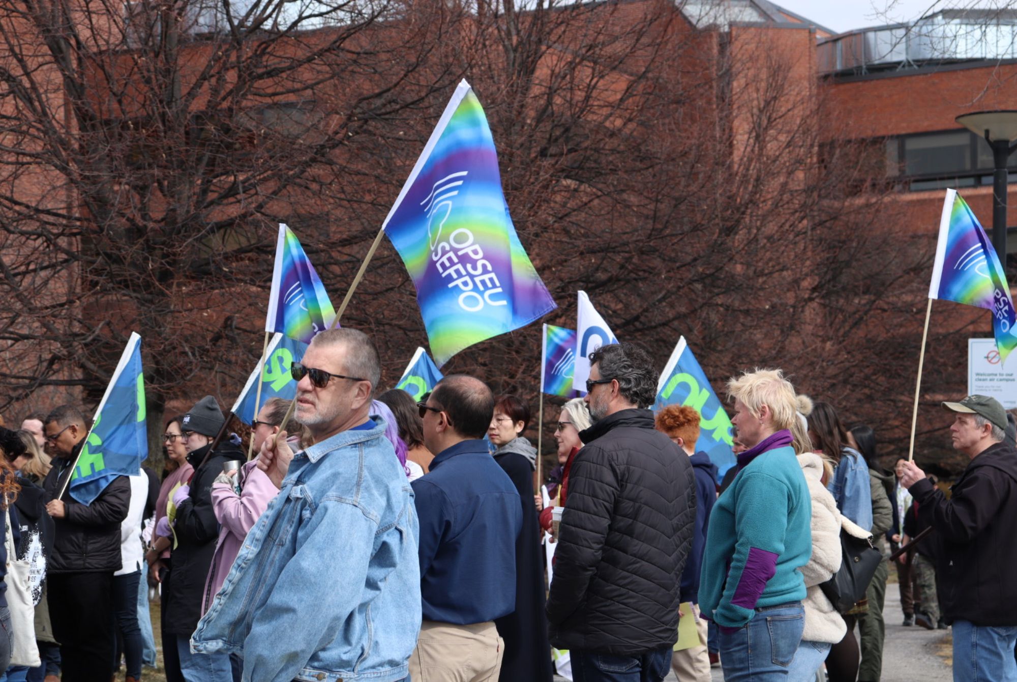 Demonstrators gather, holding flags and signs at the Show Your Work rally on March 10 at Algonquin College.