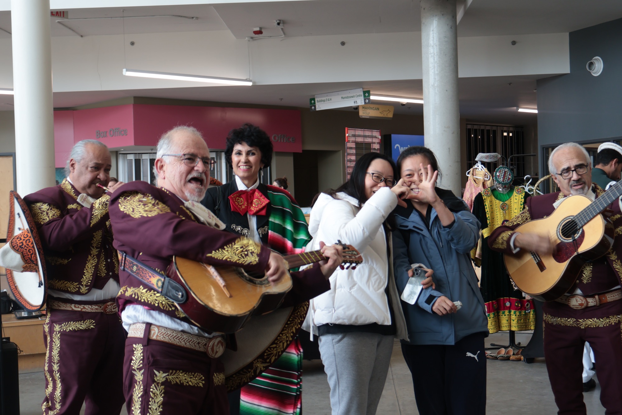 A mariachi group performs as two attendees stop for a photo in the middle of the celebration.